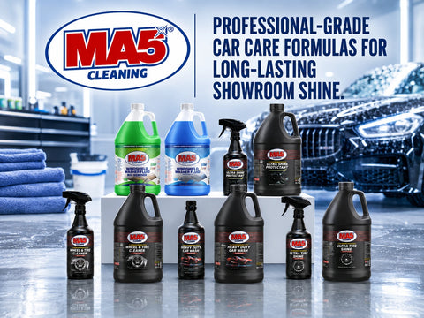 A group of MA5X car cleaning products arranged on a white platform in a showroom setting, with a blue car and cleaning towels in the background. The products include various bottles and sprayers in black, green, and blue packaging.